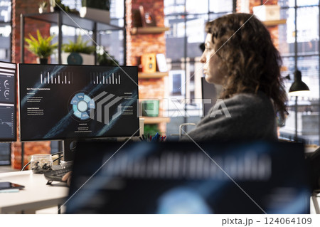 Young company analyst at office watching business presentation on PC display, reviewing statistics charts and performance metrics. Employee looking at presentation graphs on computer. 124064109