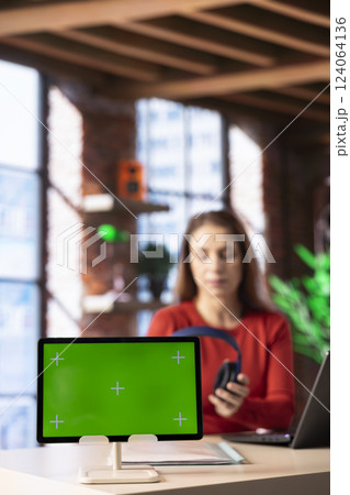 Adult setting up headphones to listen to a podcast while she works next to mockup, helping her to focus on her freelance work tasks at home office. Woman tech savvy finishes a gig remotely. 124064136