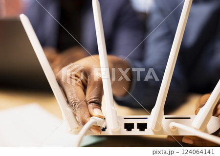 Young black woman pulling out the LAN cable from the modem while her boyfriend reads a technical manual on laptop for troubleshooting. Wi-Fi reset to fix connectivity issues. Close up. 124064141