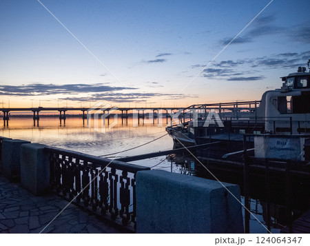 【ウクライナ】東部ドニプロの河川沿岸に係留された船と橋がある日没直後の夕景 124064347