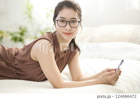 ベッドでくつろいでスマホを見る若い女性 124066472