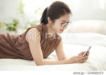 ベッドでくつろいでスマホを見る若い女性 124066473