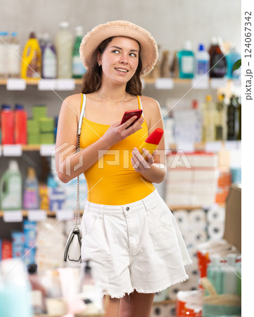 Young female shopper scanning barcode on bottle of tanning lotion with phone 124067342