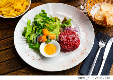 Tartar beef with quail egg and arugula served on plate. Modern French cuisine Tartar beef with quail egg and arugula served on plate. Modern French cuisine 124067410