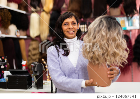 Latin american woman choosing natural hair wig at specialty boutique Latin american woman choosing natural hair wig at specialty boutique 124067541
