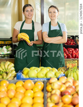 Happy two female sellers wearing apron and standing next to organic foods in supermarket Happy two female sellers wearing apron and standing next to organic foods in supermarket 124067884