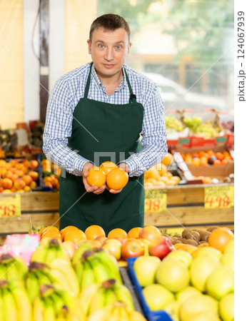 Friendly salesman offering ripe oranges in fruits and vegetables store Friendly salesman offering ripe oranges in fruits and vegetables store 124067939