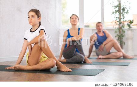 Portrait of sporty teen girl practicing Matsyendrasana known as Lord of Fishes Pose during yoga training with family Portrait of sporty teen girl practicing Matsyendrasana known as Lord of Fishes Pose during yoga training with family 124068196