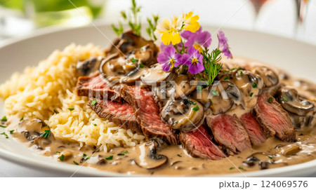 Gourmet beef stroganoff with sliced medium-rare steak, creamy mushroom sauce, and fragrant rice, elegantly garnished with edible flowers and fresh herbs on a white plate 124069576