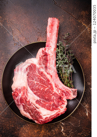 Fresh Tomahawk beef steak, raw marbled rib eye with bone on plate with herbs. brown background. top view 124070035