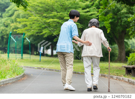 杖を使うシニア女性と介護士の後ろ姿 124070182