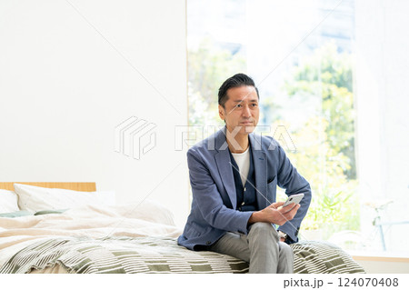 ベッドでスマホを見るミドル男性 124070408
