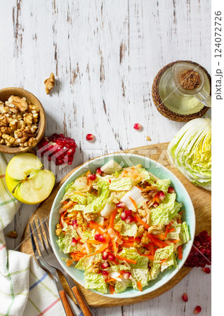Dietary salad fresh vegetable of Chinese cabbage, carrots, apple, nuts and pomegranate with vinaigrette dressing on a white wooden table. Top view flat lay. Copy space. 124072726