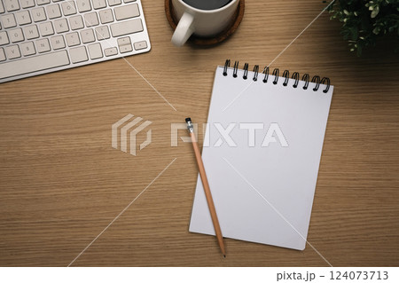 Top view of wooden desk with blank spiral notebook, keyboard and a cup coffee 124073713