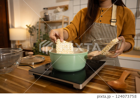 Close up shot of woman putting dried instant noodles into a boiling pot Close up shot of woman putting dried instant noodles into a boiling pot 124073758