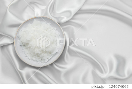 Magnesium flakes in a bowl resting on elegant white silk fabric 124074065