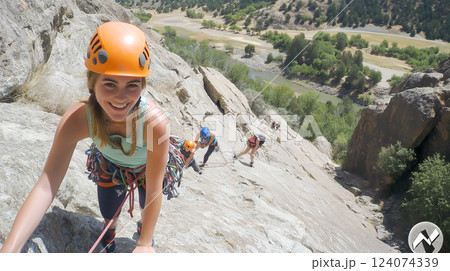 Climbers ascend a rocky cliff with stunning views of the river and landscape in a sunny outdoor adventure Climbers ascend a rocky cliff with stunning views of the river and landscape in a sunny outdoor adventure 124074339