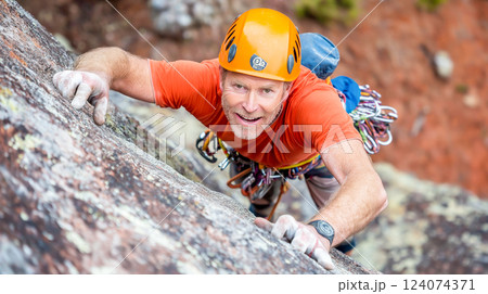 Skilled climber scaling a rocky face in a mountainous with safety gear and climbing equipment 124074371