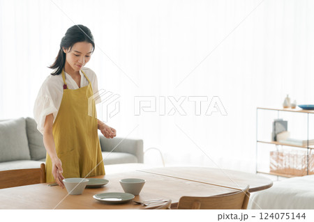 食器を食卓に並べるエプロンの女性 124075144