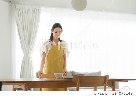 食器を食卓に並べるエプロンの女性 124075148