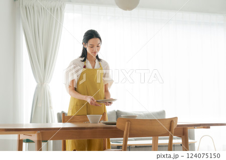 食器を食卓に並べるエプロンの女性 食器を食卓に並べるエプロンの女性 124075150