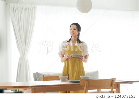 食器を食卓に並べるエプロンの女性 124075153