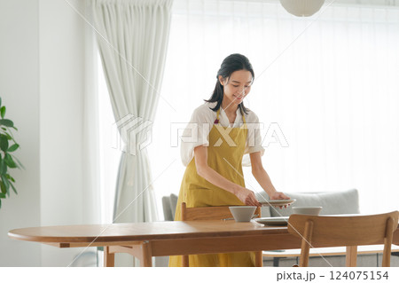 食器を食卓に並べるエプロンの女性 食器を食卓に並べるエプロンの女性 124075154