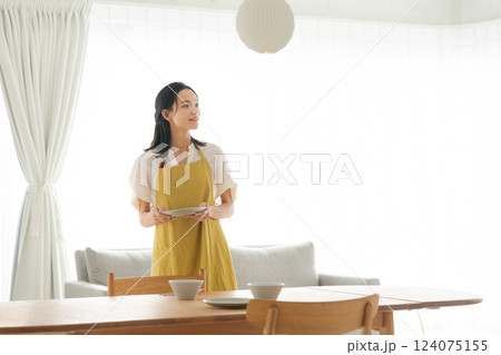 食器を食卓に並べるエプロンの女性 124075155
