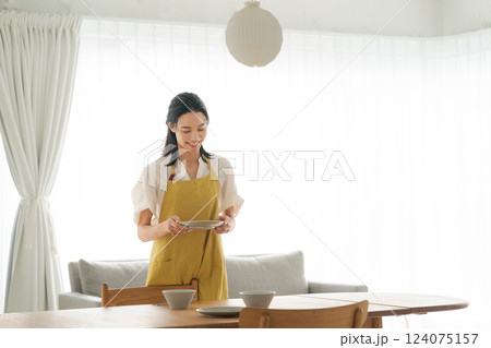 食器を食卓に並べるエプロンの女性 食器を食卓に並べるエプロンの女性 124075157