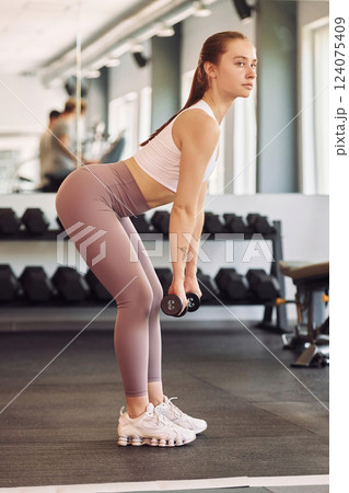 Side view. Lifting dumbbells. Young beautiful woman in sportive clothes have fitness day in the gym 124075409