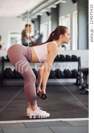 Side view. Lifting dumbbells. Young beautiful woman in sportive clothes have fitness day in the gym 124075410