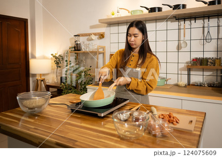 Young Asian woman preparing meal on an Induction stove in a kitchen 124075609