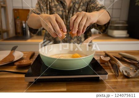 Close up shot of man cracking an egg into a frying pan, ready to prepare delicious meal Close up shot of man cracking an egg into a frying pan, ready to prepare delicious meal 124075611
