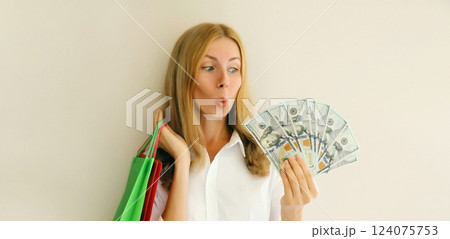 Surprised shocked young woman with shopping bags holding cash money looking at dollar bills Surprised shocked young woman with shopping bags holding cash money looking at dollar bills 124075753