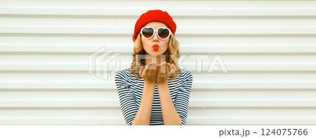 Portrait of beautiful happy young woman blowing a kiss in red french beret, heart shaped sunglasses 124075766