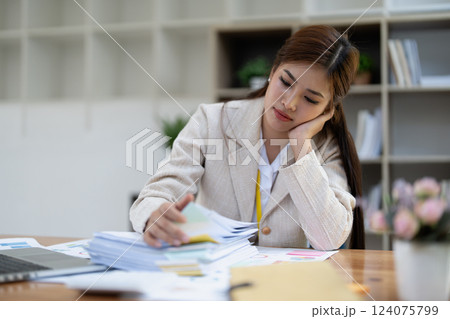 Stressed young businesswoman overwhelmed by paperwork with finance, market charts and documents in office Stressed young businesswoman overwhelmed by paperwork with finance, market charts and documents in office 124075799