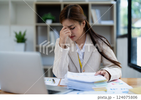 Stressed young businesswoman overwhelmed by paperwork with finance, market charts and documents in office Stressed young businesswoman overwhelmed by paperwork with finance, market charts and documents in office 124075806