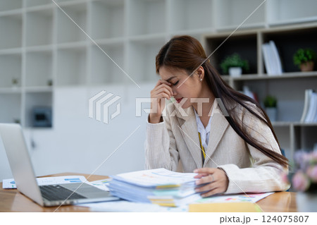 Stressed young businesswoman overwhelmed by paperwork with finance, market charts and documents in office 124075807