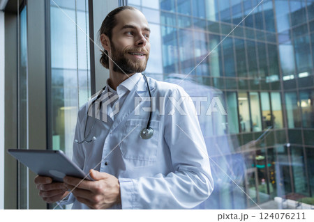 Male healthcare worker standing near window in hospital using modern technology 124076211