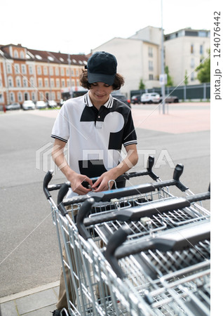 Young guy taking trolley at store unfastening cart for purchase during sale Young guy taking trolley at store unfastening cart for purchase during sale 124076442