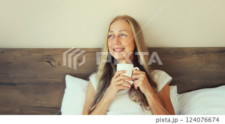 Happy smiling mature woman enjoying with cup of hot coffee lying on bed at home 124076674