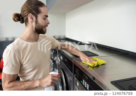 Man cleaning washer with detergent after using at laundromat Man cleaning washer with detergent after using at laundromat 124076789