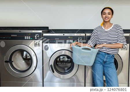 Woman using self-service washing machine in public laundromat washing dirty laundry for hygiene Woman using self-service washing machine in public laundromat washing dirty laundry for hygiene 124076801