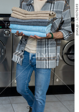 Unrecognizable man in laundromat holding towels after using commercial washer Unrecognizable man in laundromat holding towels after using commercial washer 124076849