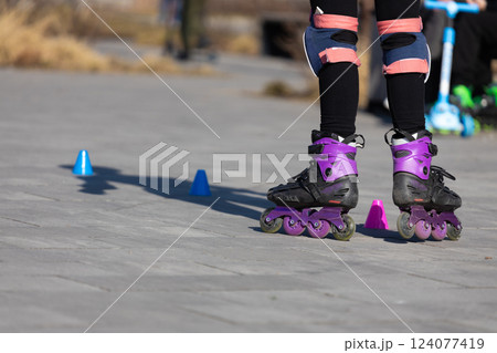 A close-up view of rollerblading in action showcasing an individual wearing purple inline skates, practicing skills using colorful cones on a sunny day outdoors. 124077419