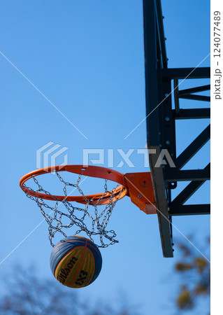 Basketball in Motion: A Close-Up View of a Wilson Basketball About to Score Through an Orange Hoop Under a Clear Blue Sky Basketball in Motion: A Close-Up View of a Wilson Basketball About to Score Through an Orange Hoop Under a Clear Blue Sky 124077489
