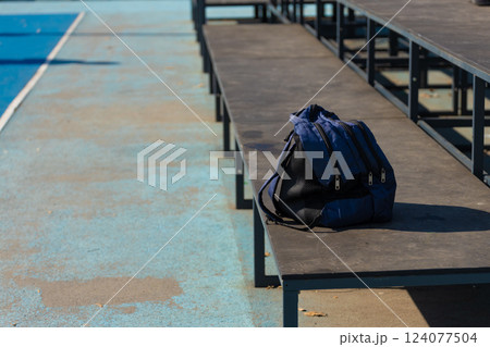 Lonely Backpack on a Sports Bench: A Captivating Scene Depicting Tranquility in an Outdoor Sports Environment Lonely Backpack on a Sports Bench: A Captivating Scene Depicting Tranquility in an Outdoor Sports Environment 124077504