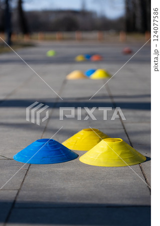 Colorful Training Cones on a Smooth Pavement in a Bright Outdoor Setting, Ideal for Sports Practice and Skill Development Activities in a Park Environment 124077586