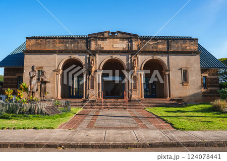The Kauai Museum in Lihue, Hawaii features a classical facade with three arches, ornate columns, a statue, brick pathways, and a clear blue sky. The Kauai Museum in Lihue, Hawaii features a classical facade with three arches, ornate columns, a statue, brick pathways, and a clear blue sky. 124078441