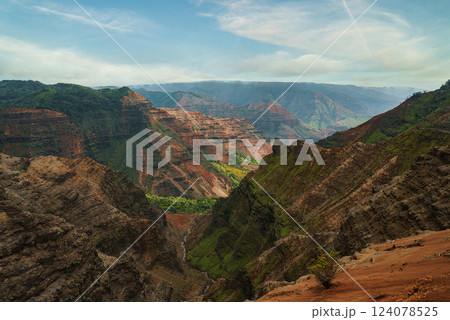 View of Waimea Canyon on Kauai, Hawaii, featuring red cliffs, green valleys, a winding stream, and layered rock formations under a clear blue sky. View of Waimea Canyon on Kauai, Hawaii, featuring red cliffs, green valleys, a winding stream, and layered rock formations under a clear blue sky. 124078525